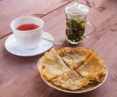 Fincan çay ve bir tabak krep yerken üzerine ahşap bir masa ile