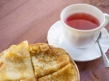 Fincan çay ve bir tabak krep yerken üzerine ahşap bir masa ile