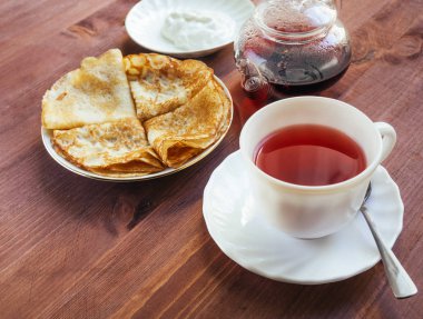 Fincan çay ve bir tabak krep yerken üzerine ahşap bir masa ile