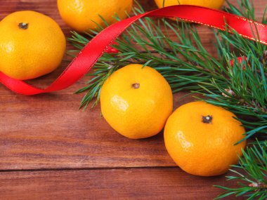 Bir Noel ağacı ve ahşap arka plan üzerinde kırmızı kurdele dalları ile mandalina