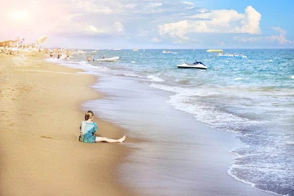 Mavi yumuşak dalgalar Altın kum üzerinde rulo, kız sahilde kum da oynar.