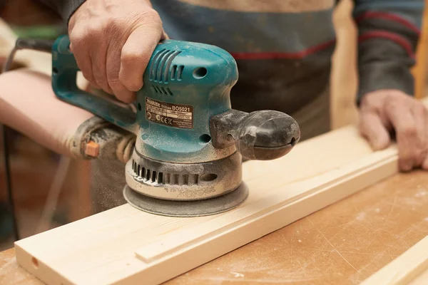 Bir adam bir taşlama makinesi ile ahşap bir ürün davranır.