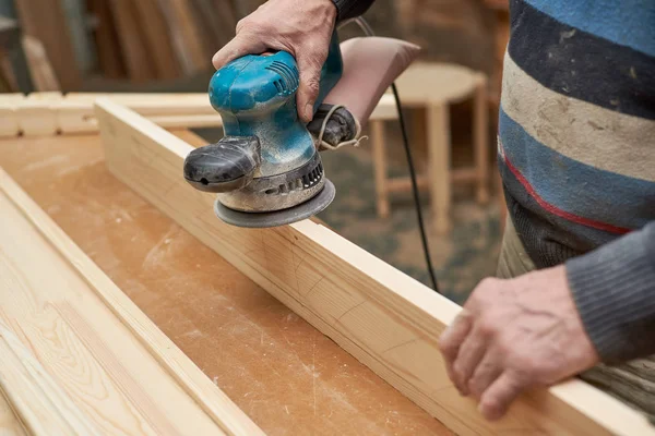 Bir adam bir taşlama makinesi ile ahşap bir ürün davranır.