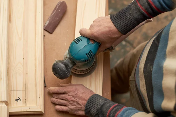 Ένας άνθρωπος μεταχειρίζεται ένα ξύλινο προϊόν με μια μηχανή λείανσης. — Φωτογραφία Αρχείου