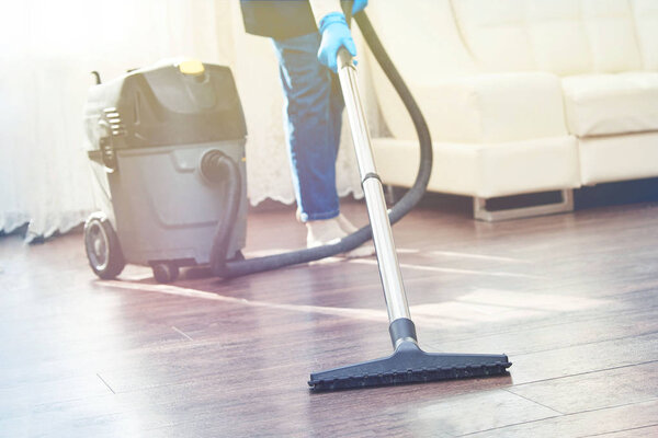 Girl vacuuming floors in the room near the sofa industrial vacuum cleaner