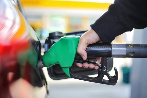 Close up hand holding green gasoline fuel nozzle and being fill gas tank of black car in gas station Concept of Global Fossil Fuel Consumption.  Replace by alternative energy in near the near future