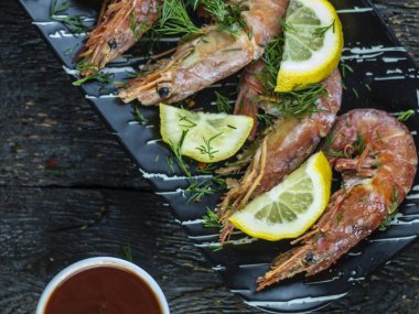 Ahşap bir arka plan üzerinde limon, yeşillik ve sos ile Haşlanmış karides.