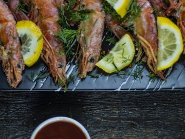 Ahşap bir arka plan üzerinde limon, yeşillik ve sos ile Haşlanmış karides.