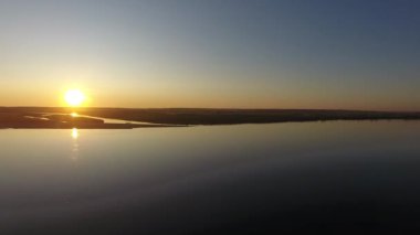 Kamera gün batımına doğru nehir ve alan üzerinde uçar. Güneş batıyor, hava sessiz.