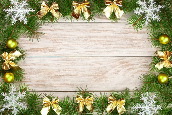 Marco de Navidad hecho de ramas de abeto decoradas con copos de nieve y arcos dorados sobre un fondo de madera claro — Foto de Stock