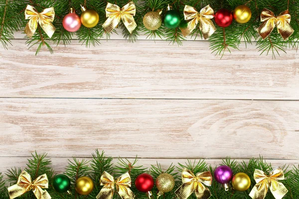 Moldura de Natal feita de ramos de abeto decorados com bolas e arcos em um fundo de madeira leve — Fotografia de Stock