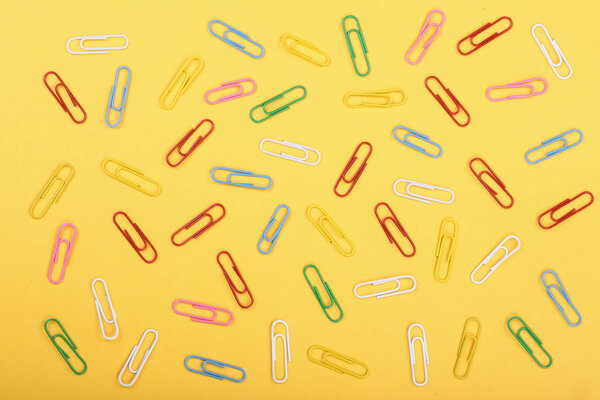 colorful paper clips on yellow background. Top view. Flat lay pattern