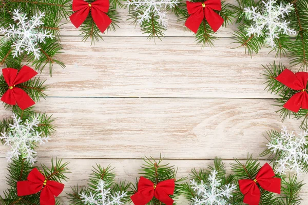 Χριστουγεννιάτικο καρέ από κλαδιά έλατου διακοσμημένα με νιφάδες χιονιού και κόκκινα τόξα σε ανοιχτόχρωμο φόντο ξύλινη — Φωτογραφία Αρχείου