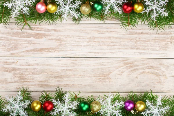 Рождественская рама из еловых ветвей, украшенных снежинками и шарами на светлом деревянном фоне — стоковое фото