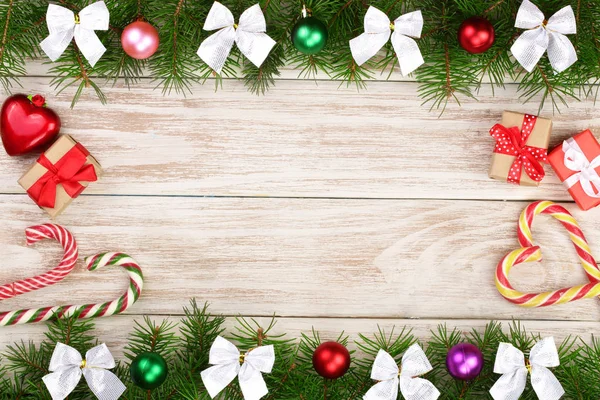 Moldura de Natal feita de ramos de abeto decorados com bolas, arcos, bastões de doces e caixas em um fundo de madeira leve — Fotografia de Stock