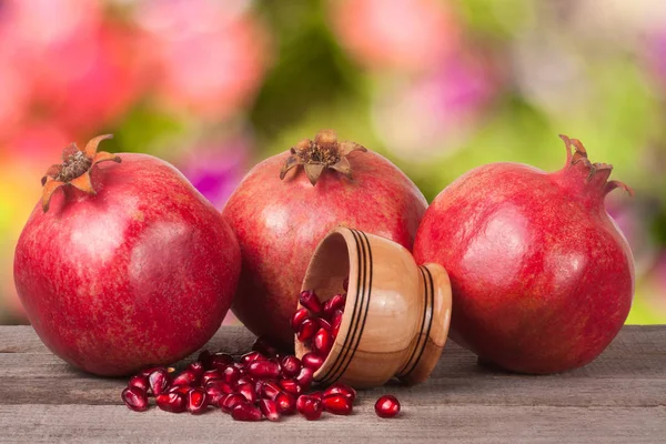 Three pomegranate and garnet grains in a bowl on wooden table with blurred garden background — Stock Photo, Image