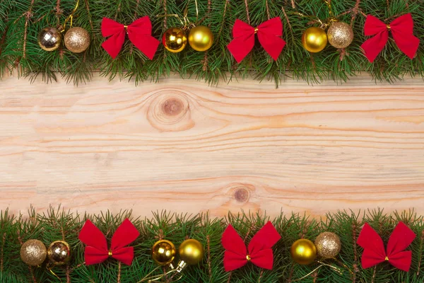 Рождественская рама из елки, украшенная красными луками и золотыми шариками на светлом деревянном фоне — стоковое фото