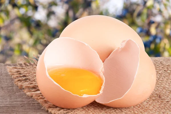 Broken egg with yolk and eggshell On a wooden table with a blurry garden background — Stock Photo, Image