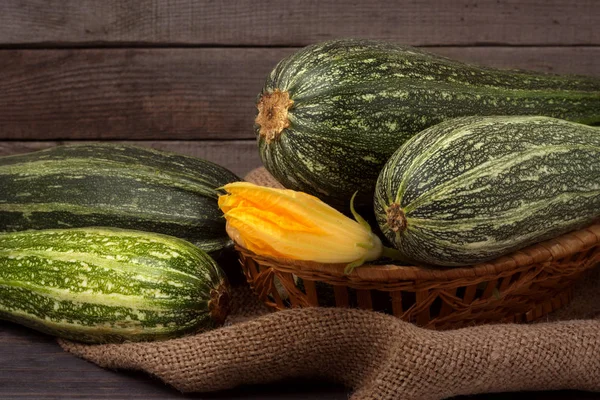 Green zucchini or courgettes with a flower on sackcloth wooden background — Stock Photo, Image