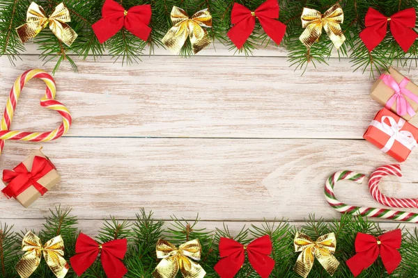 Moldura de Natal feita de ramos de abeto decorados com arcos, bengalas de doces e caixas em um fundo de madeira leve — Fotografia de Stock