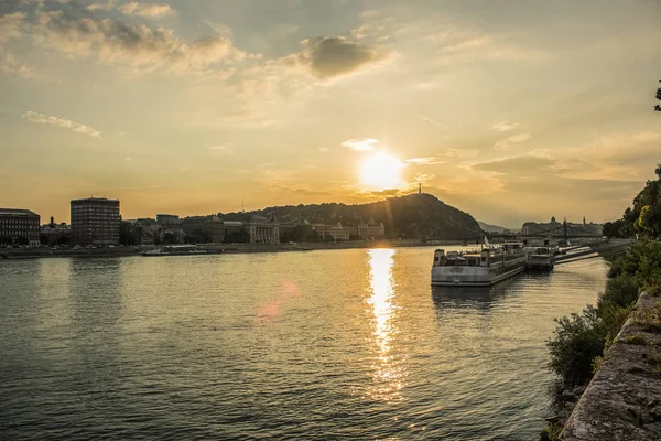 Budapeşte waterfront kentsel city scape ile Tuna Nehri günbatımı zamanında gemiler ve güneş bakıyor