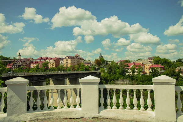 Ukraine European medieval city urban landmark photography with symmetry marble fence and columns foreground, many colorful small houses and green trees with blue sky and white clouds background