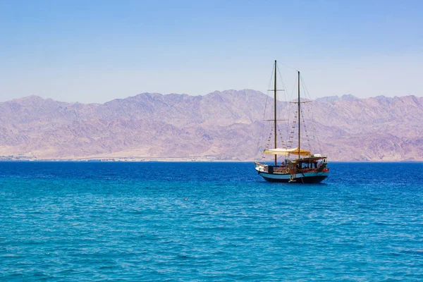 cruise tourism on a sea summer season scenic landscape picture of vintage wooden ship floating on water in Persian Guld near Saudi Arabia desert mountains waterfront