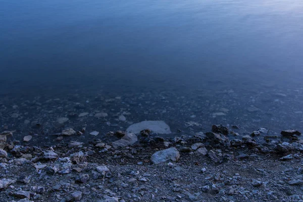 长曝光水自然简单的背景水平壁纸模式的石头海滨和光滑的水面在傍晚蓝色黄昏时间与空间复制或文本 — 图库照片