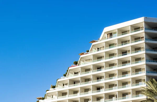 resort hotel building apartment exterior architecture facade with windows and terraces on a roof foreshortening from below on blue sky background , copy space