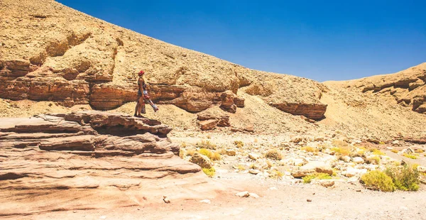 Israeli travel photography in desert scenic landscape environment near entrance to Red canyon touristic destination with Caucasian woman in long dress stay on small cliff