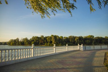 yumuşak renklerde döşeli yol ve beyaz çit ile yürüyüş ve gezinti için rahat nehir sahil park bölgesi erken sonbahar sezonu hava 