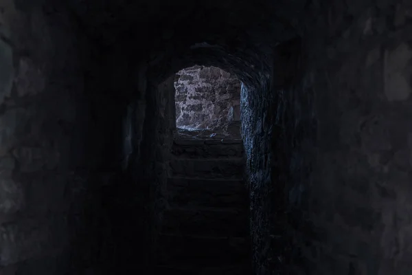 creepy medieval castle corridor stone indoor alley path way between cold walls in twilight shadow with exit light view