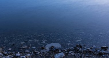 gün batımından sonra akşam alacakaranlık aydınlatma sakin pürüzsüz su yüzeyi ile uzun pozlama taş sahil şeridi manzara manzara görünümü basit doğa arka plan, metin için kopya alanı