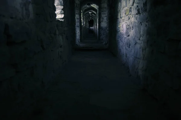 ancient fortification corridor indoor narrow passage between stone walls in twilight blue toning lighting with many shadows