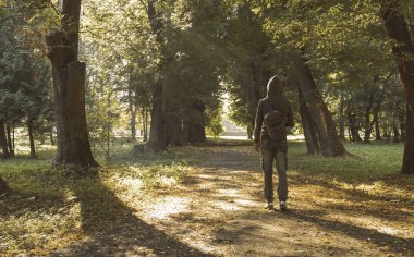 sabah parkı yeşillikleri ile güneş doğma ışınları geri kameraya hoodie bilinmeyen yürüyüş adam ile alley yol yolda düşen