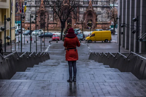 autumn rainy cloudy cold weather time and girl in coat stay back to camera on concrete gray stairs in back street alley of Ukrainian capital Kyiv