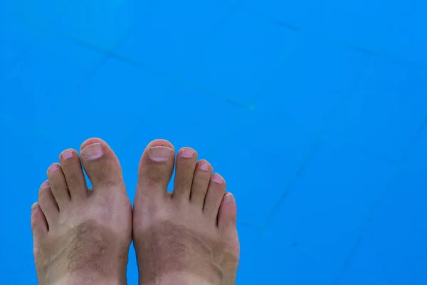male feet with funny tan above smooth blue water background surface of swimming pool, relaxation concept wallpaper picture with empty copy space