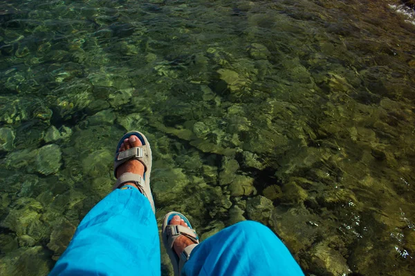boy feet in blue sandals above lake green water