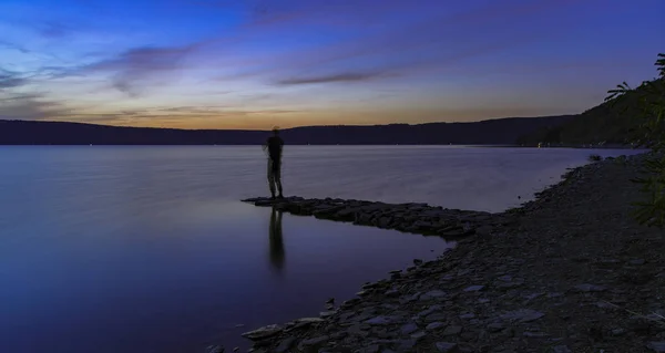 abstract unfocused human silhouette fishing life style hobby action in peaceful twilight lake shore line scenic landscape after sunset, concept long exposure photography with empty copy space