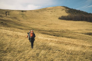 Dağ yürüyüşü konsept seyahat fotoğraf afişi sırt çantalı turistin kameraya geri dönüşü resimli dağlık İskoçya manzaralı doğa manzarası, uzay kopyası 
