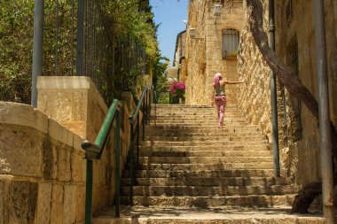 İsrail 'in kutsal şehri Kudüs eski sokak dar merdivenleri ve kameraya geri dönen kız kutsal yerdeki antik taş duvarlara dokunuyor. 
