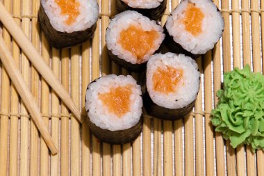 Ev yapımı suşi rulo maki, çiğ somon balığı ve ahşap sopalarla geleneksel halı ve wasabi malzemesi.