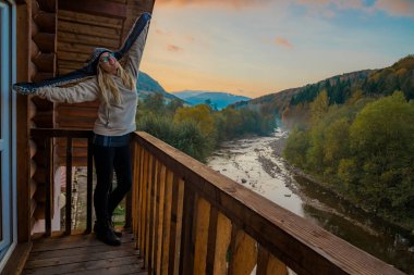 Sonbahar dağ ormanlarında ve nehir manzarasında poz veren bir kız. Sabah güneşinin doğuşu manzarası. Hafif sisli hava, otel balkon yeri.