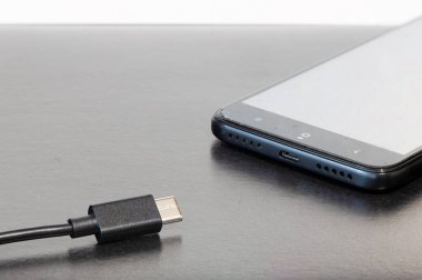 Ofis masası cep telefonu ve şarj aleti kriko ve kablosu gri arkaplan yüzeyi. Metnin için boş kopya alanı var.