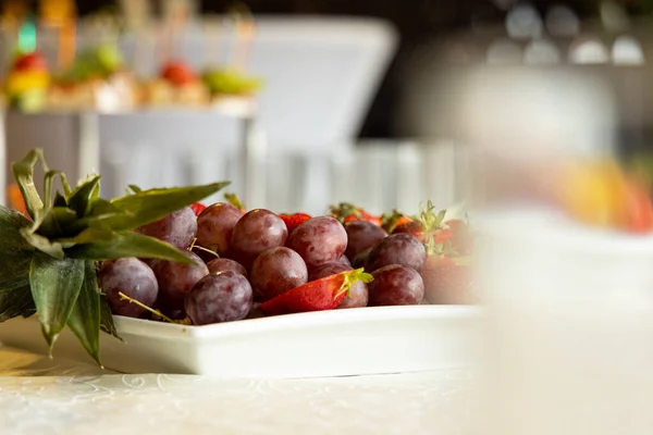 白テーブルクロスと料理のテーブルの上のブドウの新鮮なフルーツプレートディナーフード写真ビューフォーカスされていない前景グレアコンセプトヘルスケアライフスタイルを食べる — ストック写真