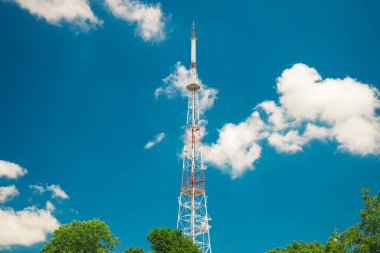Yüksek TV kulesi altyapısı nesnesi aşağıdan canlı mavi gökyüzü arkaplanı ve açık hava fotoğrafçılığının yeşil yaprakları üzerinde öngörü yapıyor.