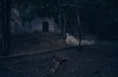 Cadılar Bayramı konsepti resmi. Kale yakınlarında taklitçi bir hayalet. Gece vakti ormanda harabeler, koyu mavi tonlama tarzı.