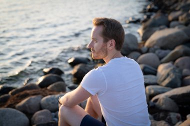 Gün batımında okyanus kenarında genç bir adamın portresi.