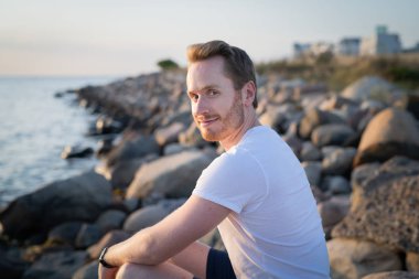 Gün batımında okyanus kenarında genç bir adamın portresi.