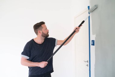 Adam duvara açık gri boya sürüyor.